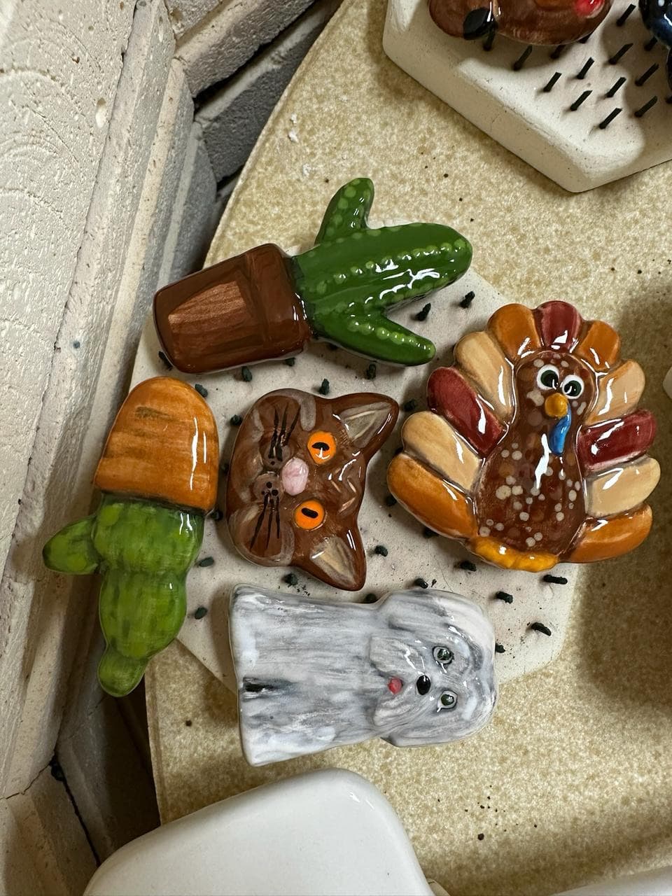 Glazed animal tiles — cat, turkey, cactus, carrot — displayed on wood board at MADE @ The Local pottery studio in Centerville, TN