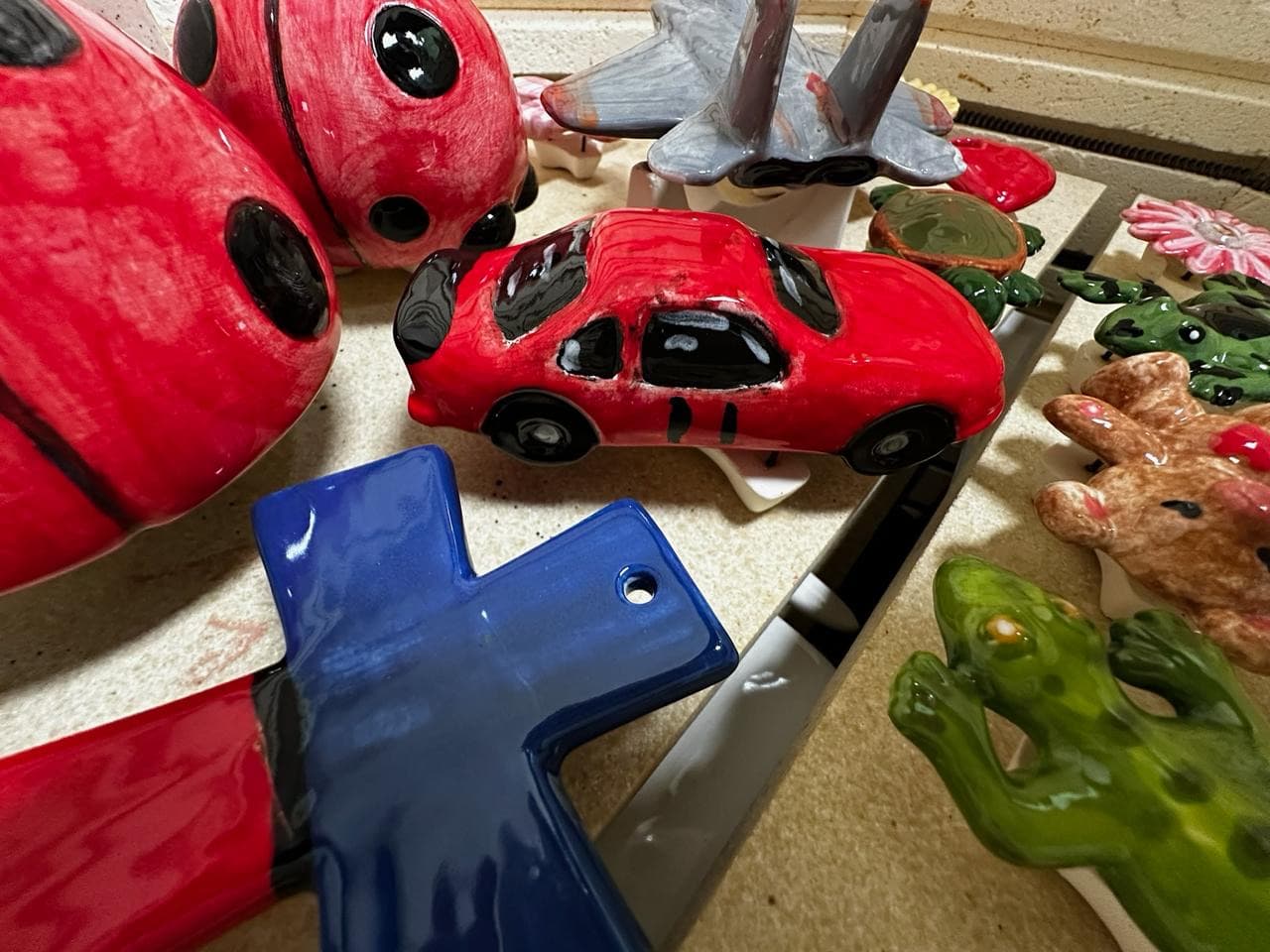 Colorful finished pottery pieces including ladybugs, cars, and frogs on display shelf at MADE @ The Local pottery studio in Centerville, TN